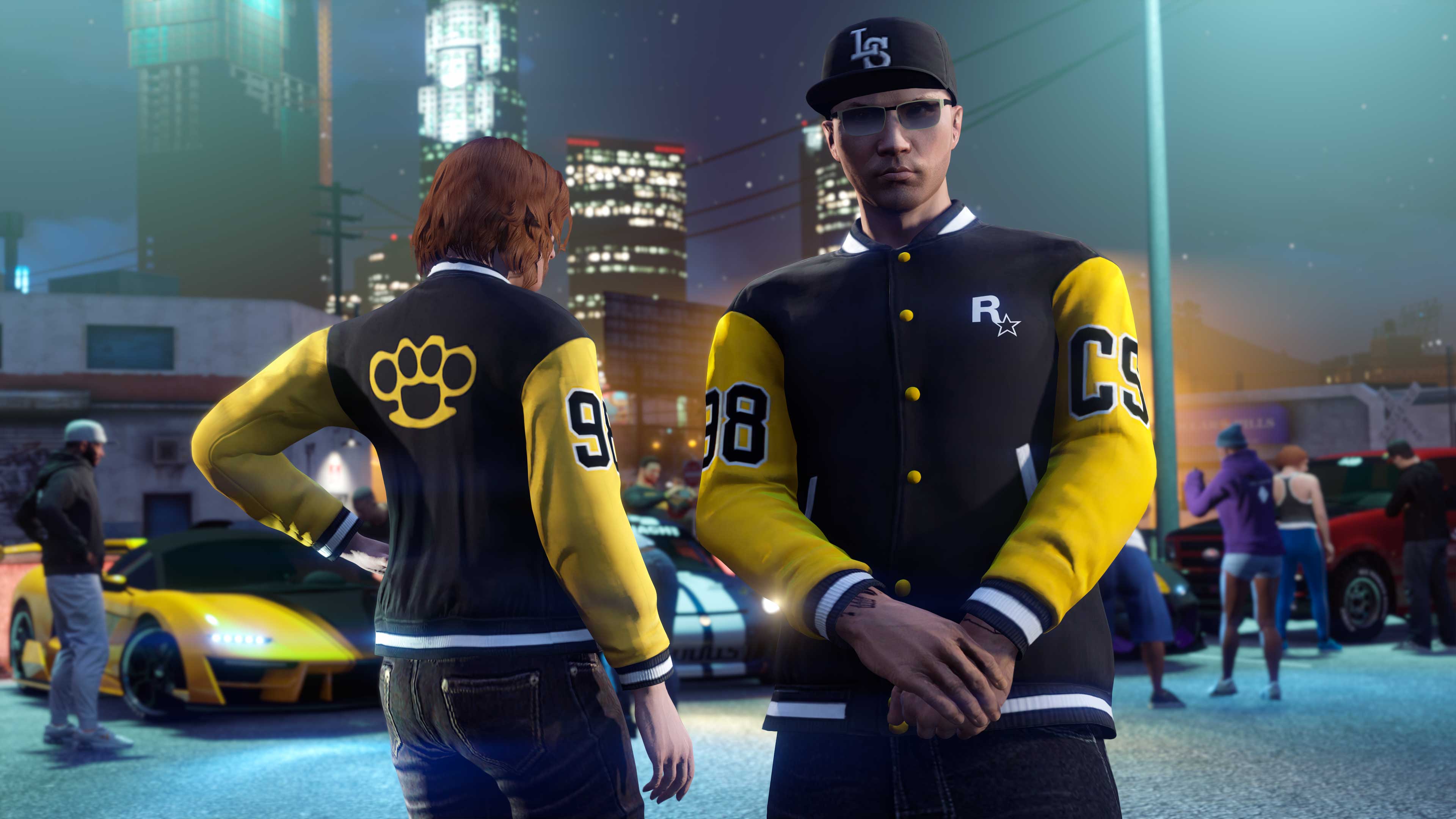 Two GTA Online characters wearing the Community Series Varsity Jacket at a car meet. 